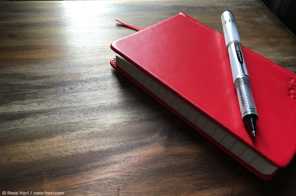 A pen rests on a red notebook