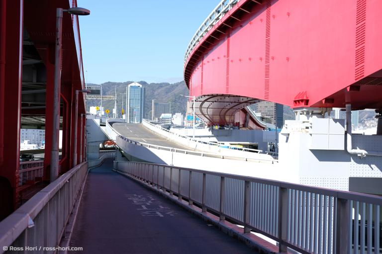 To the right the steel structure of the monorail winds off into the distance. On the left the double deck roadway. In the center, a footpath that heads down into Kobe City